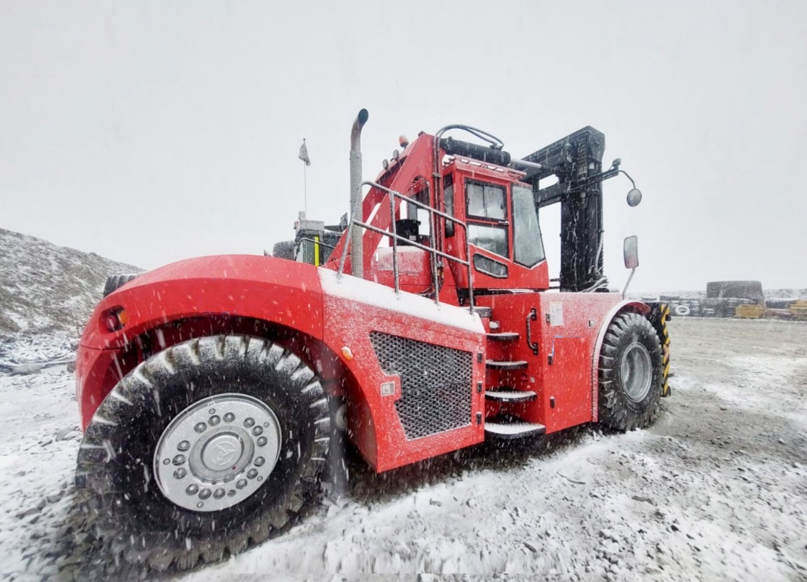 Montacargas industrial de gran tonelaje, de color rojo, operando en un área de trabajo cubierta de nieve bajo un clima de nevada.