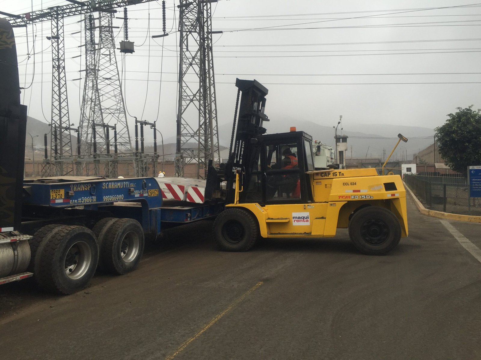 Montacargas amarillo Maquirenta de 15 toneladas, cargando un remolque Scaramucci en el exterior de una subestación eléctrica.